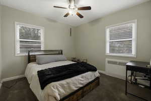 Bedroom with dark carpet, radiator heating unit, and a ceiling fan