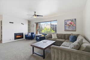 Carpeted living room with a glass covered fireplace, ceiling fan, and built in shelves