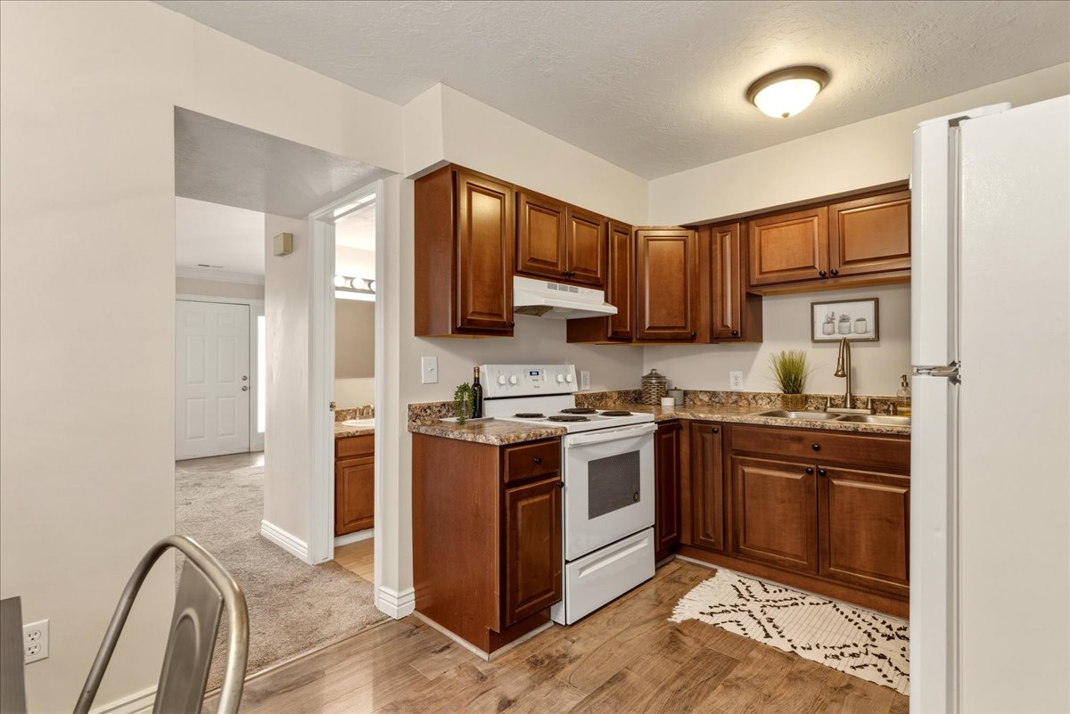 Kitchen with white appliances, light wood finished floors, light colored carpet, a textured ceiling, and wood finish cabinetry