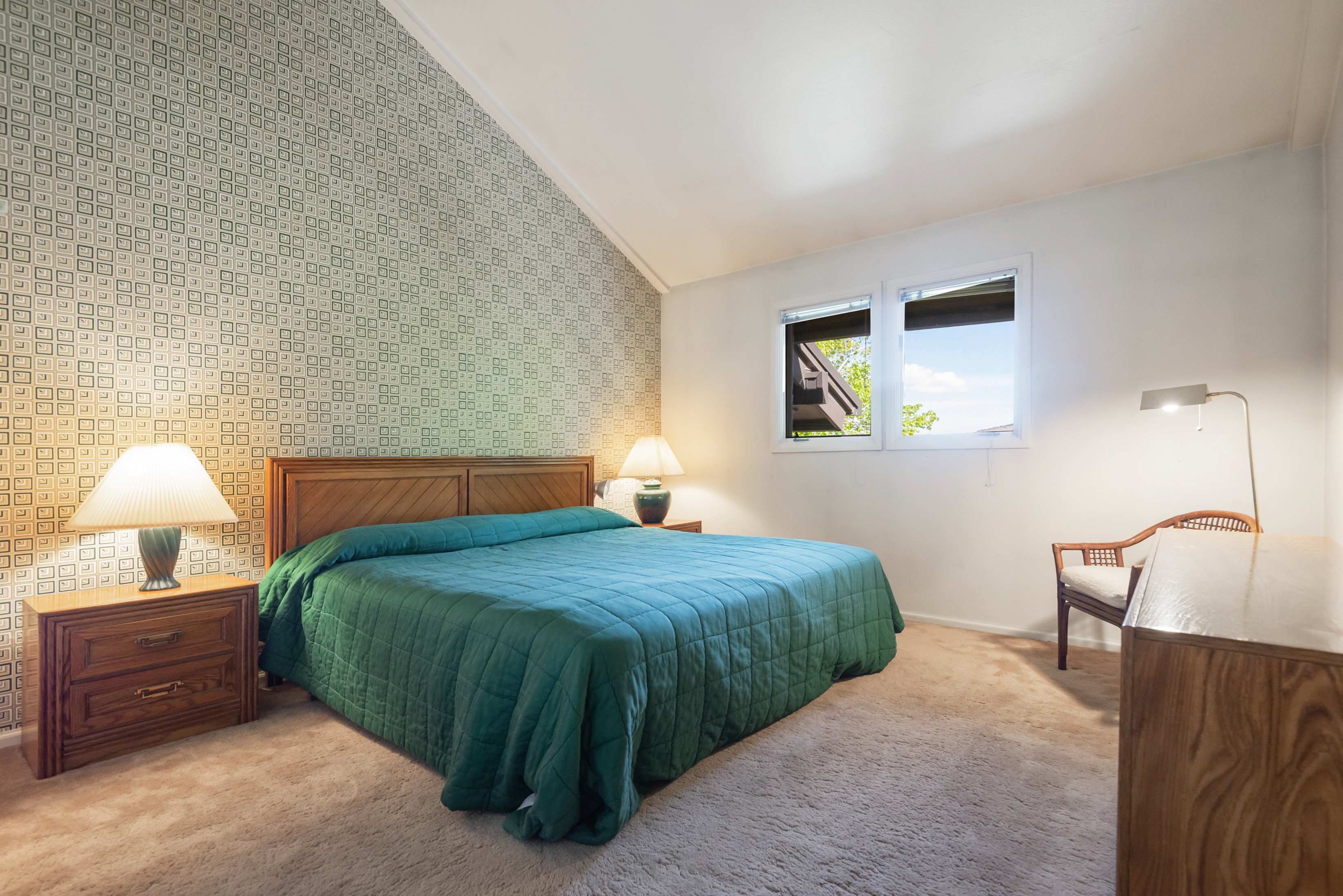 Carpeted bedroom with lofted ceiling, an accent wall, and wallpapered walls