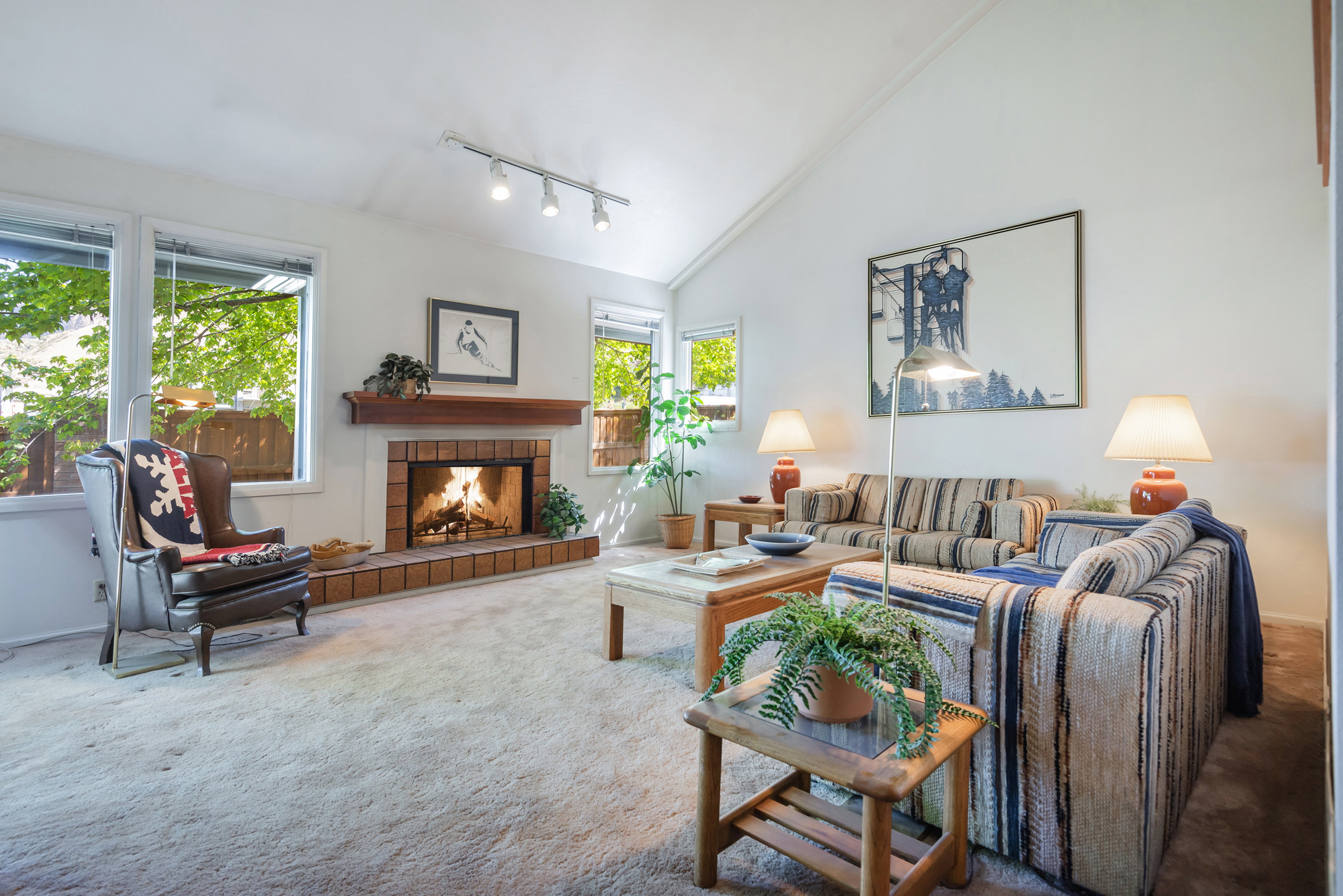 Living room featuring vaulted ceiling, carpet floors, track lighting, and a tiled fireplace