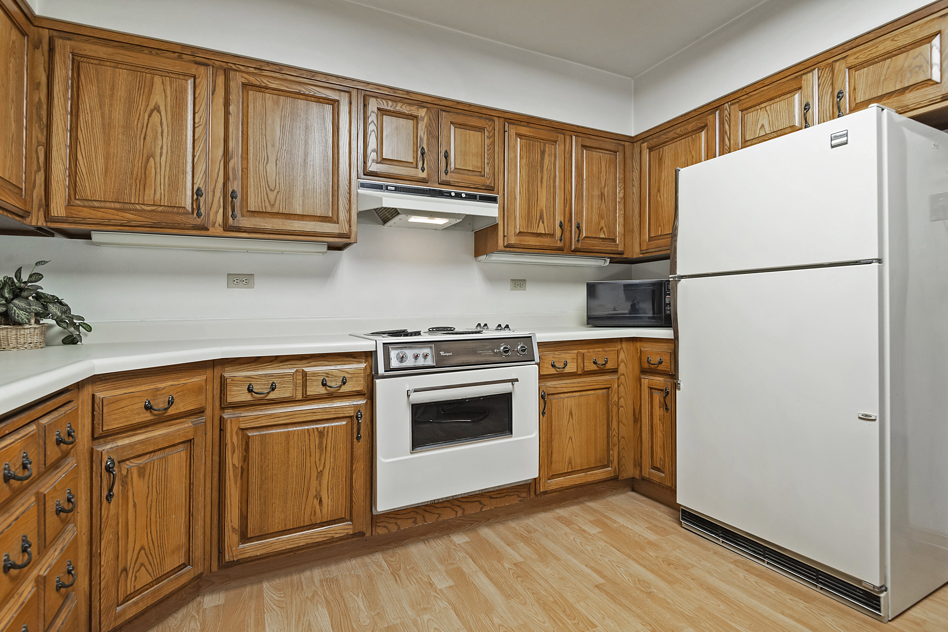 Kitchen featuring white appliances, wood finish cabinets, light countertops, and light wood-type flooring
