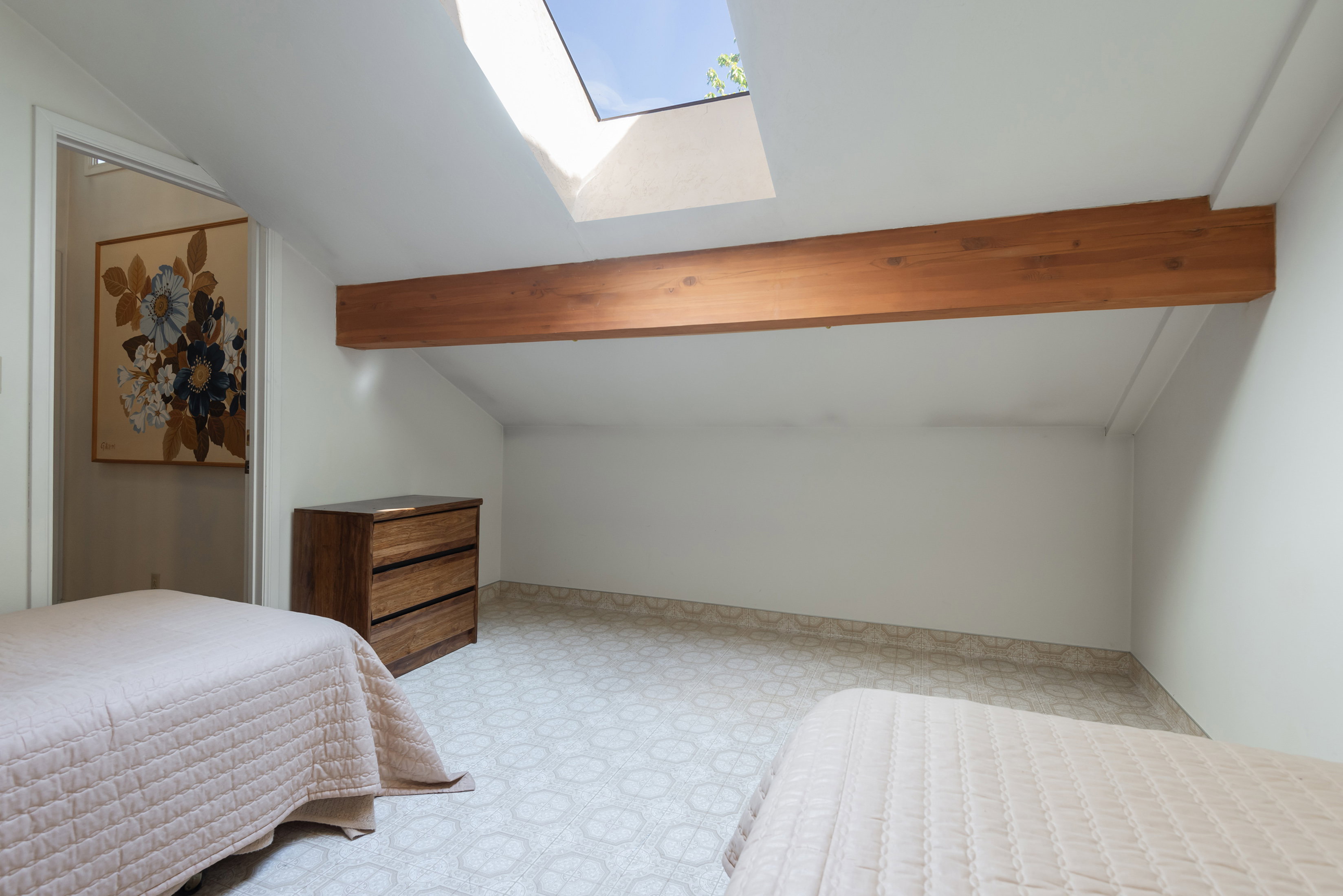 Bedroom with a skylight, vaulted ceiling with beams, and light floors