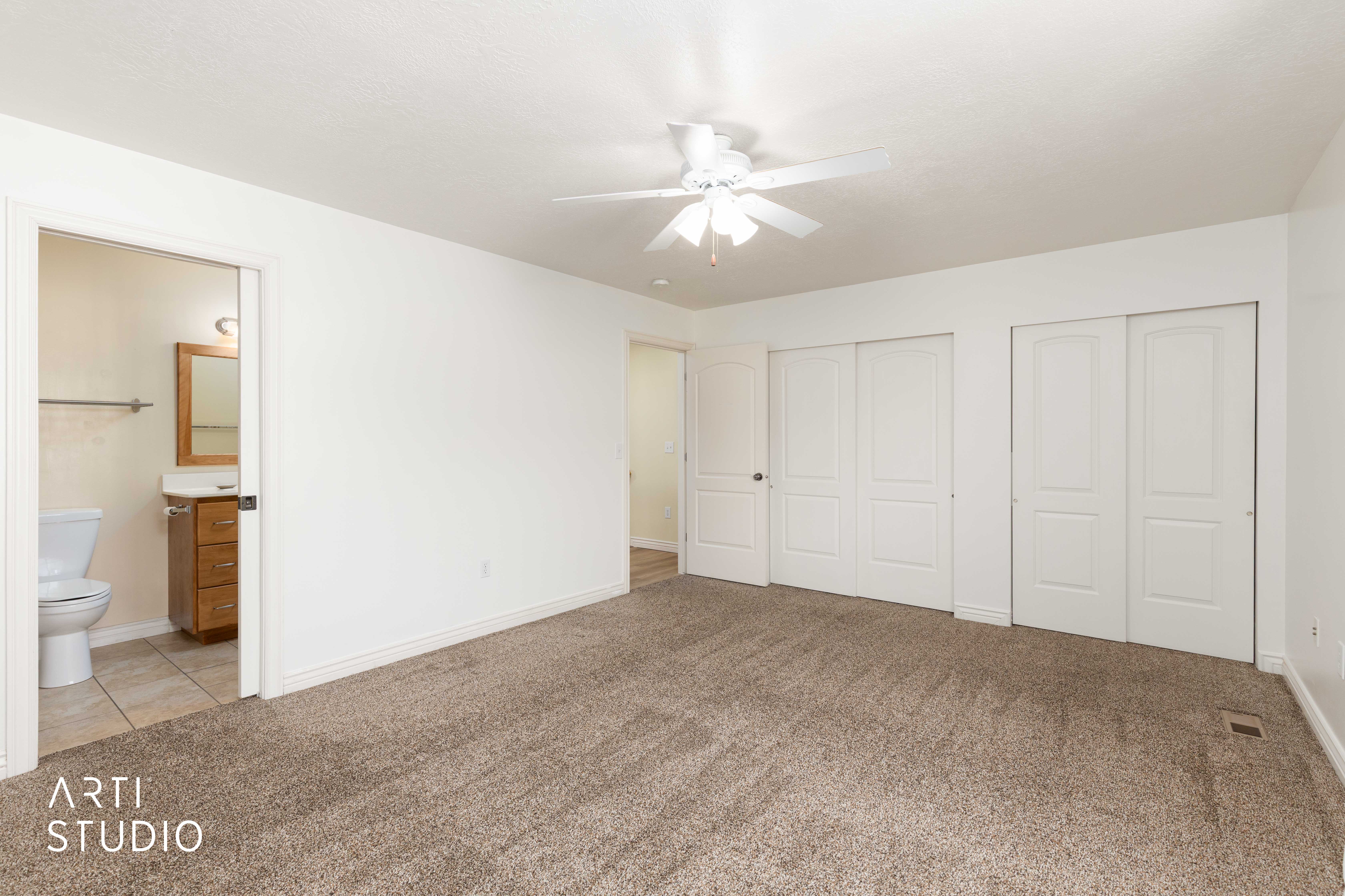 Bedroom with two closets, light carpet, connected bathroom, and a ceiling fan