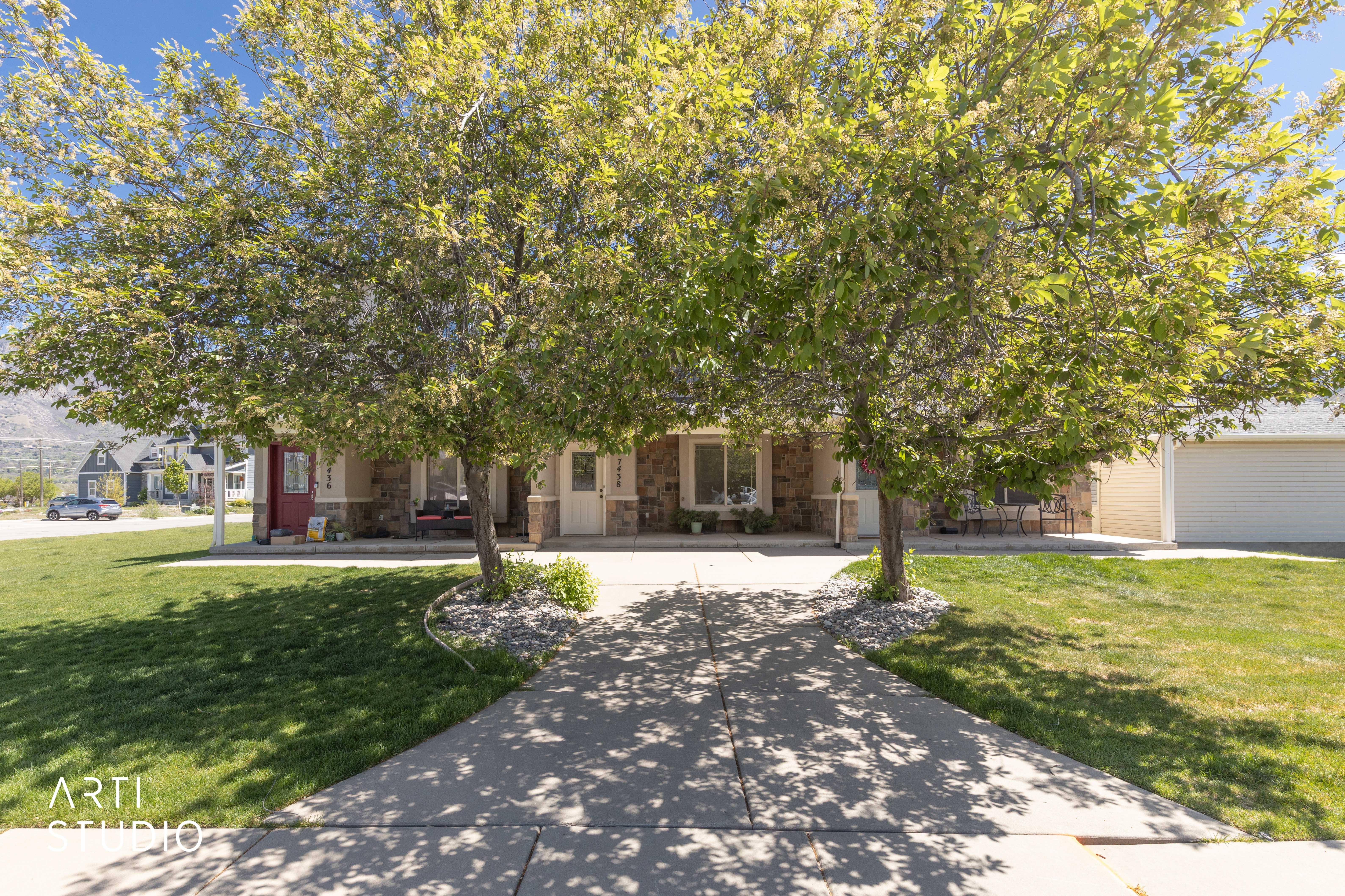 View of property behind shade trees featuring a front yard walk up sidewalk
