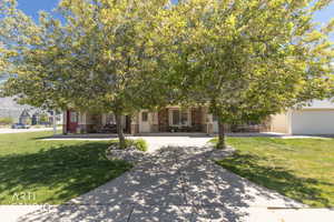 View of property behind shade trees featuring a front yard walk up sidewalk