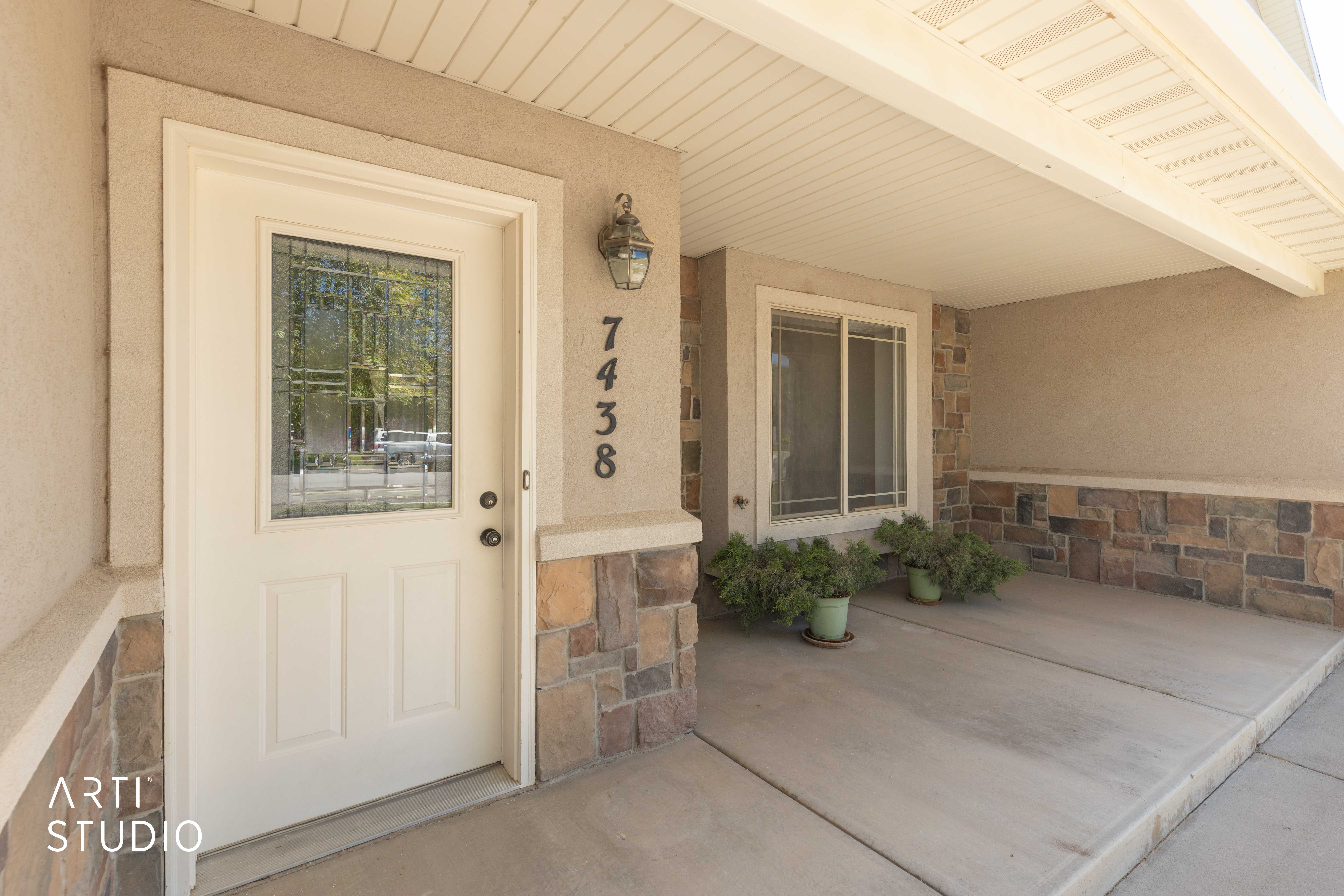 Doorway to property featuring stone siding, covered porch, and stucco siding