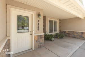 Doorway to property featuring stone siding, covered porch, and stucco siding