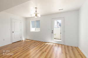 East facing back door, featuring a chandelier, light wood-style flooring, and a textured ceiling