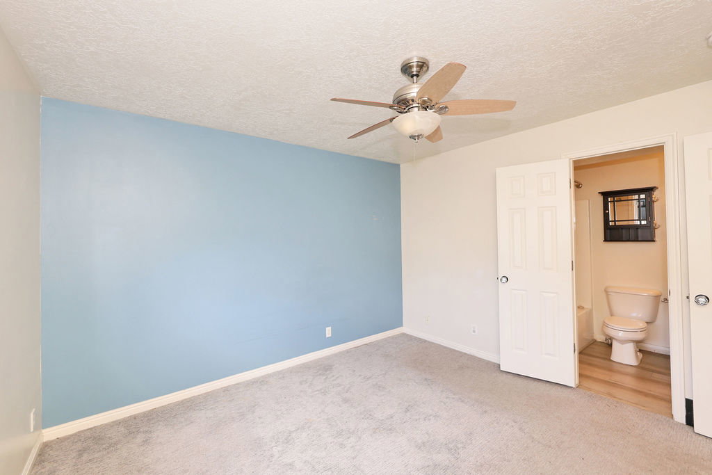 Unfurnished bedroom with a textured ceiling, light carpet, ceiling fan, and ensuite bath