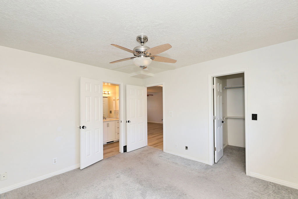 Unfurnished bedroom with a spacious closet, light colored carpet, a textured ceiling, and a ceiling fan