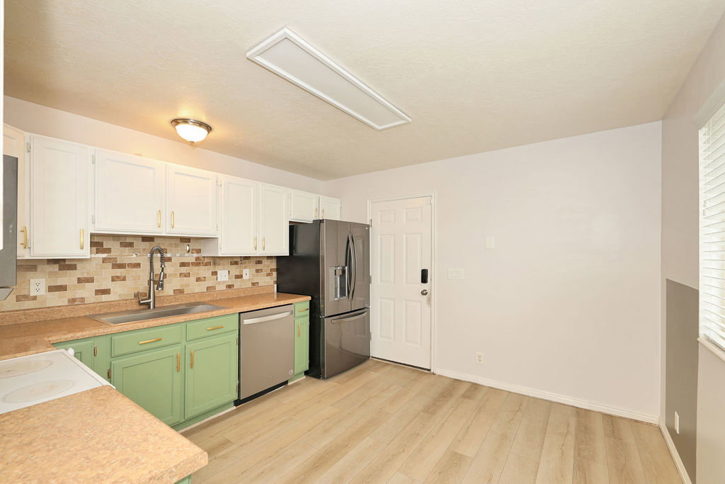 Kitchen with light countertops, two tone cabinetry, light wood-type flooring, stainless steel appliances, and backsplash