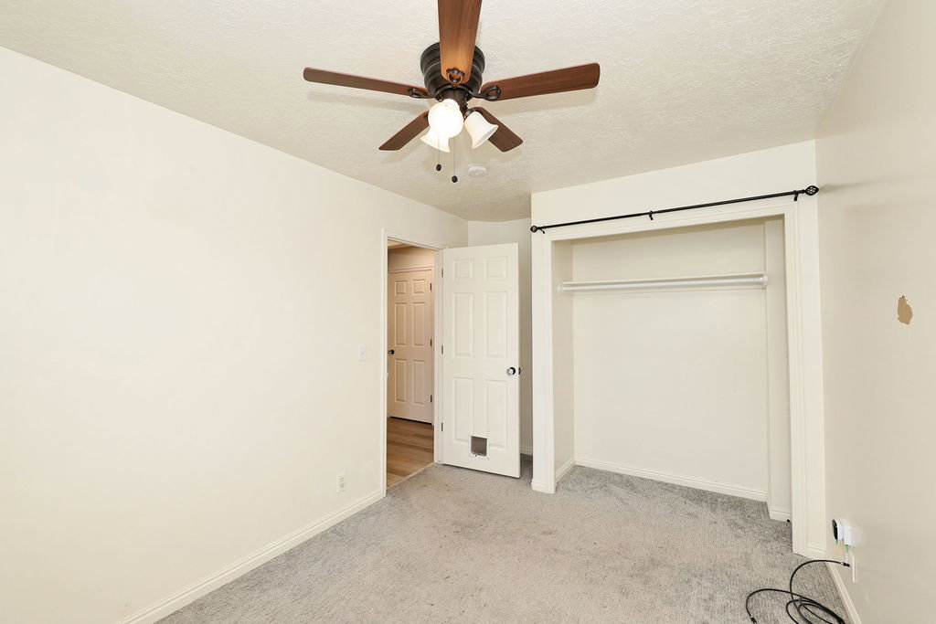 Unfurnished bedroom featuring a textured ceiling, a ceiling fan, light carpet, and a closet