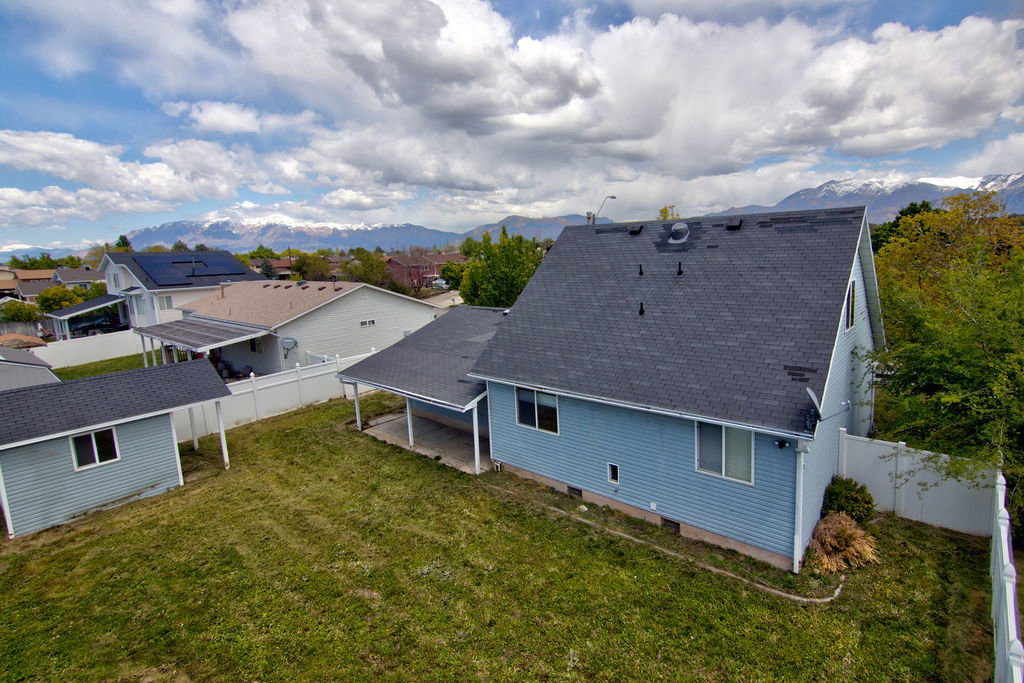 Rear view of house with roof with shingles, a mountain view, a fenced backyard, a patio, and a residential view