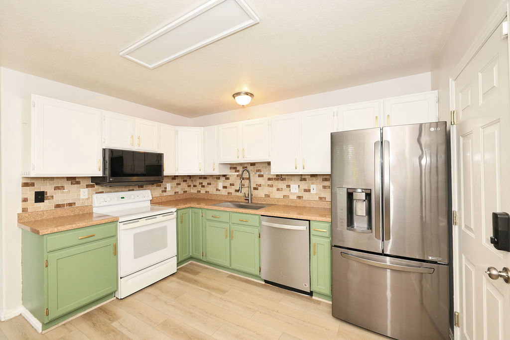 Kitchen with stainless steel appliances, light countertops, light wood-style floors, backsplash, and two tone color scheme