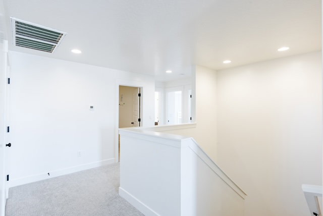 Upper level landing featuring light gray carpeting, crisp white walls, recessed lighting, and a white stair railing