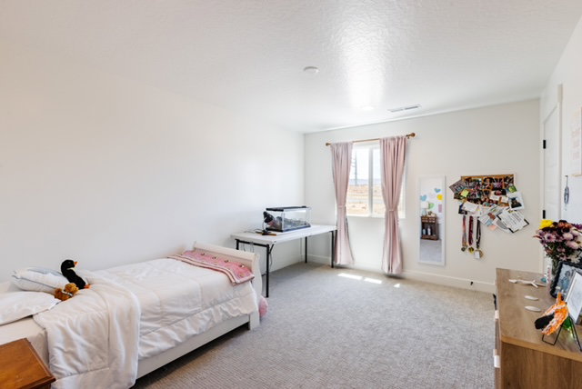 Bright room featuring light-colored carpeting, white walls, and a window with light pink drapes