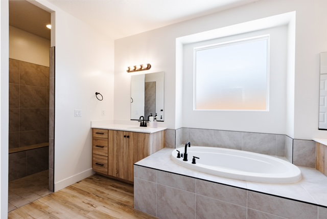 Spacious bathroom featuring a built-in soaking tub, a large window, a wood-finish vanity with a white countertop, and a walk-in shower with a built-in bench and tiled walls