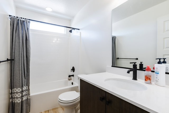 Bathroom featuring a wood-finish vanity with a white countertop and integrated sink, a large wall-mounted mirror, and a white bathtub with a tile surround