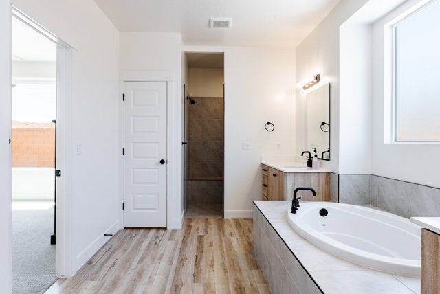 Contemporary bathroom featuring a built-in soaking tub with matte black fixtures, a dual vanity with light wood-finish cabinetry, and a walk-in shower with tile surround