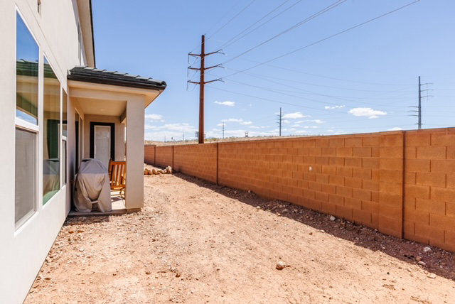 Rear exterior with an extended covered patio, a full-height block privacy wall, and an expansive unlandscaped yard