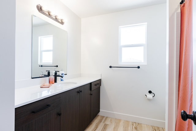 Bathroom featuring a dark wood-finish vanity with a white countertop and integrated sink, matte black fixtures, and wood-finish flooring
