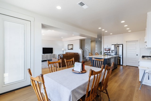 Open-concept layout featuring wood-finish flooring, recessed lighting, a kitchen island with seating, white cabinetry, and stainless steel appliances