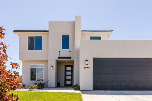 Contemporary stucco exterior with a flat roofline, featuring a dark wood-finish garage door, a modern black entry door with frosted glass panels, and exterior sconce lighting
