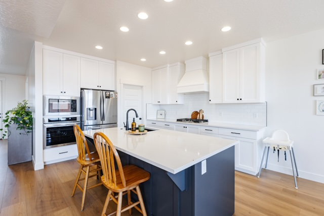 Kitchen featuring white shaker cabinetry, stainless steel appliances, a center island with a white countertop and dark base, a white subway tile backsplash, and wood-finish flooring