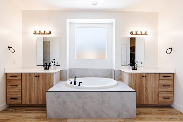 Bathroom featuring a built-in soaking tub, dual vanities with wood-finish cabinetry, white countertops, and black fixtures