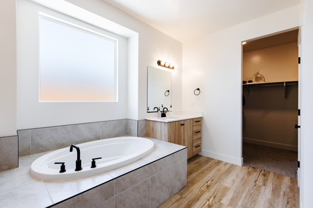 Soaking tub with matte black fixtures, set into a tiled surround with a frosted privacy window