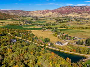 Expansive valley setting featuring a clear blue sky, distant mountains with autumn foliage, a winding road, scattered residential structures, and a prominent body of water
