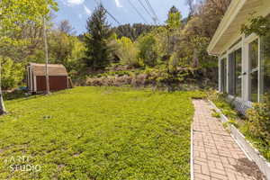 View of grassy yard featuring a storage shed and a sunroom