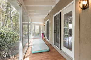 Unfurnished sunroom featuring wood finished floors, lofted ceiling with beams, and french doors