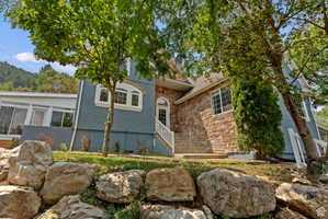 Stone and stucco exterior with multiple architectural windows, a prominent arched entry, white railing, and a tiered rock garden