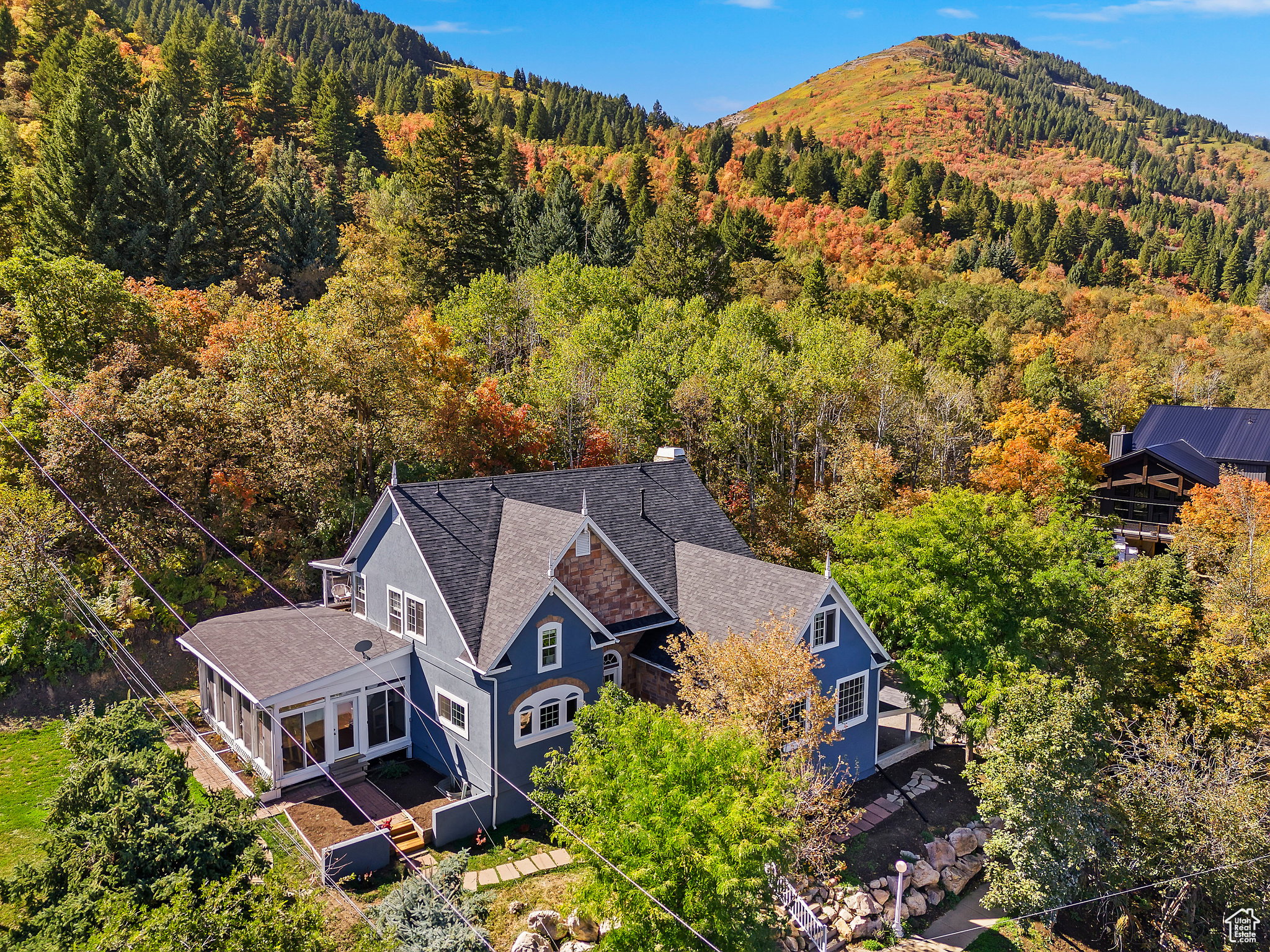 Blue exterior property featuring a sunroom, multiple rooflines, and dormer windows, complemented by surrounding mature trees and a distant mountain landscape