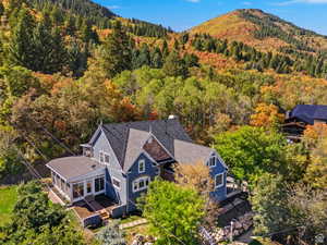 Blue exterior property featuring a sunroom, multiple rooflines, and dormer windows, complemented by surrounding mature trees and a distant mountain landscape