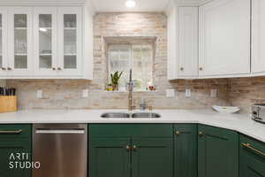 Two tone kitchen featuring dual tone cabinetry, stainless steel dishwasher, light stone counters, and glass insert cabinets