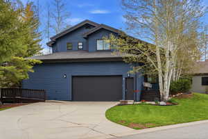 View of front of home with driveway, roof with shingles, a garage, a front yard, and a wooden deck