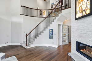 Unfurnished living room with a high ceiling, dark wood-type flooring, and a stone fireplace