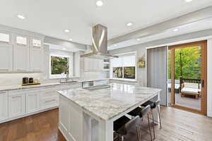 Kitchen featuring marble countertops, backsplash, dark wood finished floors, island range hood, and white cabinetry