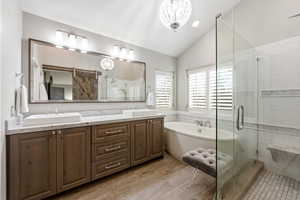 Primary Bathroom featuring vaulted ceiling, double vanity, a shower stall, a soaking tub, and suspended lighting