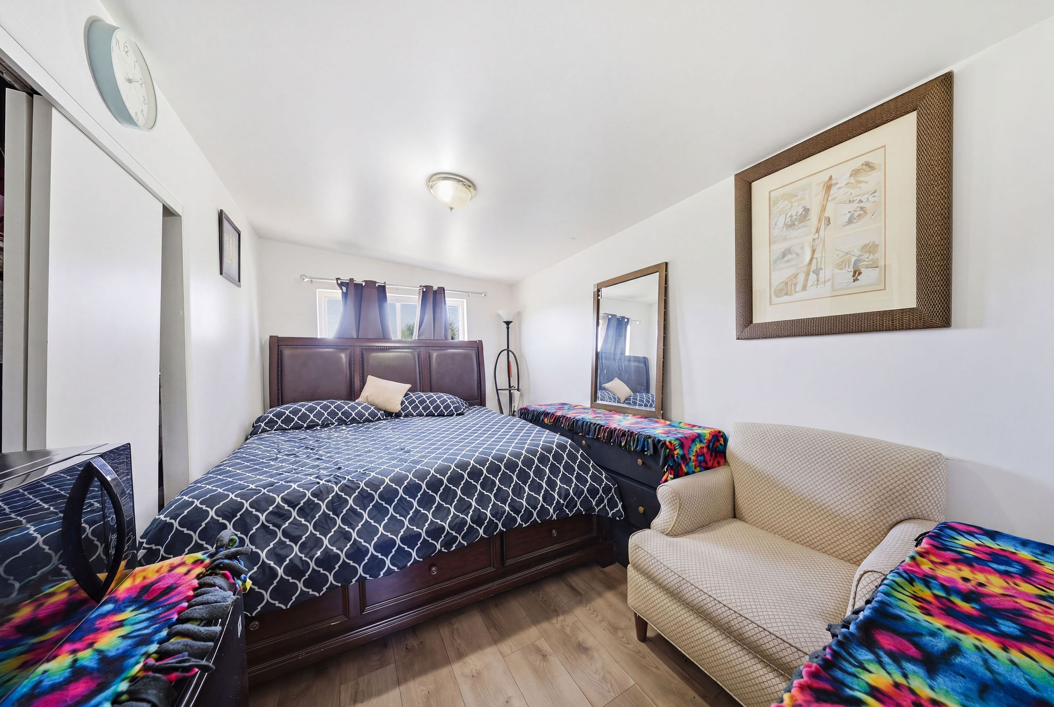 Bedroom featuring wood-finish flooring, white walls, and a window with dark curtains