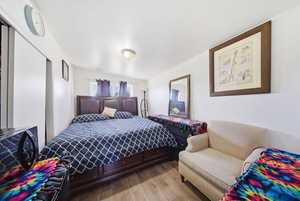 Bedroom featuring wood-finish flooring, white walls, and a window with dark curtains
