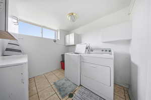 Laundry room featuring independent washer and dryer, light tile patterned floors, and cabinet space