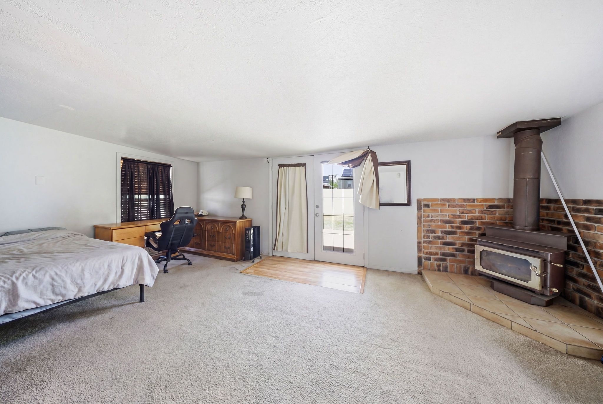 Spacious room featuring carpeted flooring, a brick accent wall with a wood-burning stove, and a glass-paned door