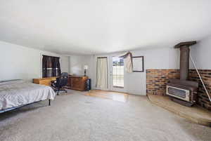 Spacious room featuring carpeted flooring, a brick accent wall with a wood-burning stove, and a glass-paned door
