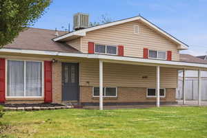 Rear view of house with a yard, brick siding, a porch, and a shingled roof