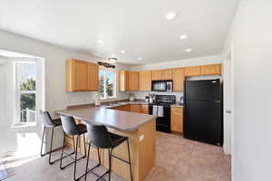 Kitchen featuring black appliances, a breakfast bar area, a peninsula, recessed lighting, and light wood finish cabinets