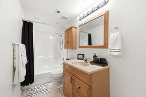 Full bath with vanity, shower / bath combo, light tile patterned floors, and a textured ceiling